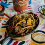 easy flank steak fajitas recipe served in cast iron skillet with peppers and onions by Muy Bueno
