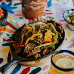 easy flank steak fajitas recipe served in cast iron skillet with peppers and onions by Muy Bueno