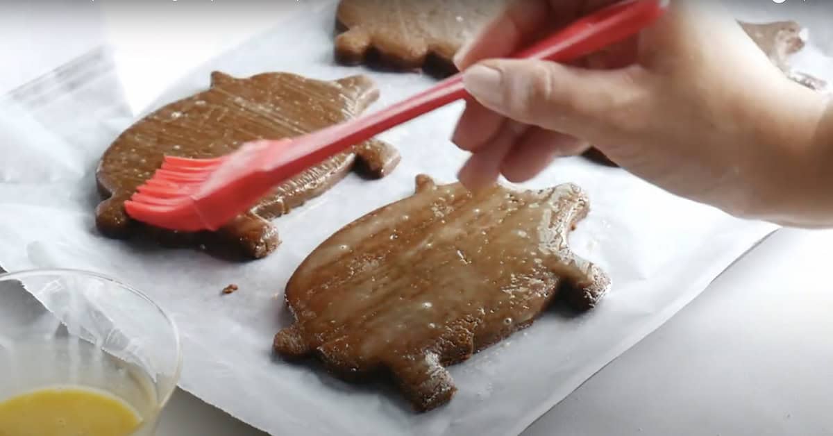 hand using a pastry brush to coat the raw cochinitos pigs with egg wash before baking. 