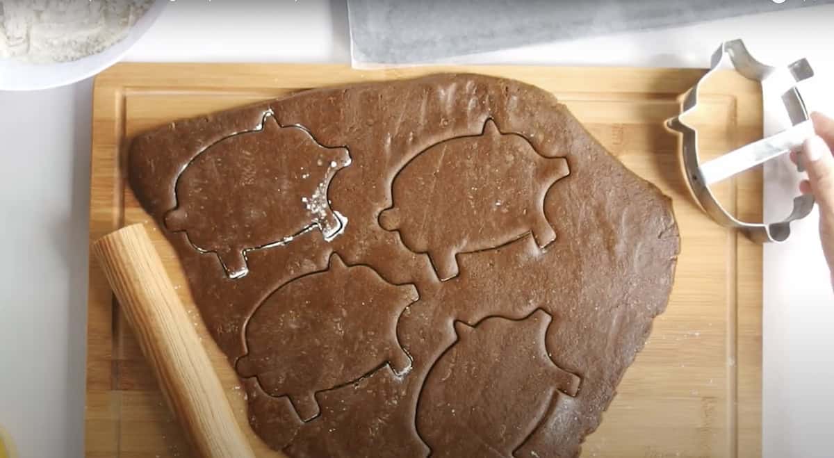 piece of rolled out marranitos dough on a wooden cutting board with 4 cut outs made with a pig-shaped cookie cutter. 