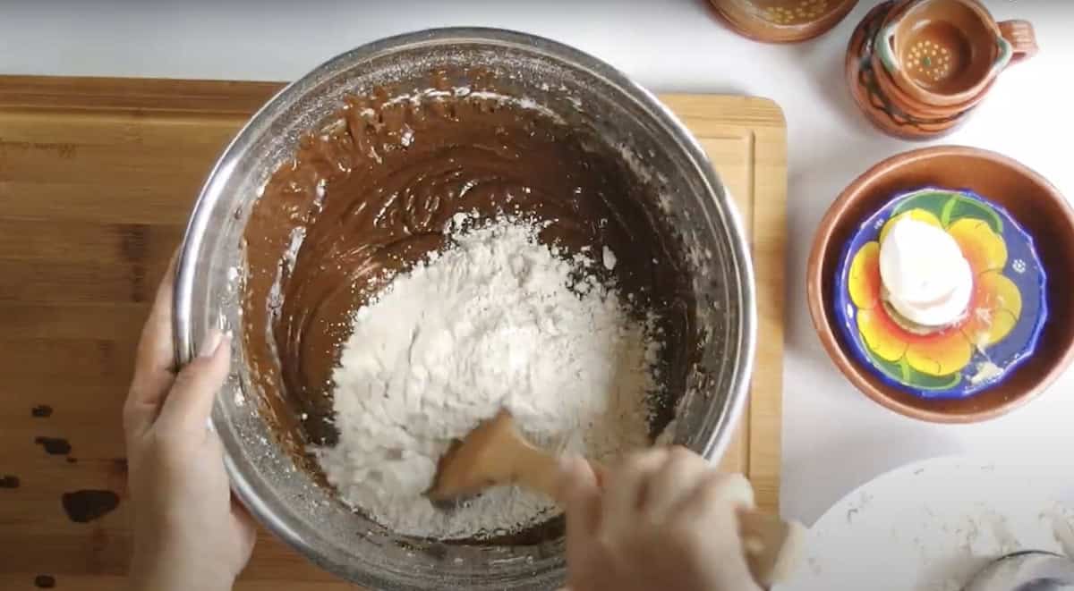 action shot of a hand folding the dry ingredients into the marranitos pan dulce dough. 