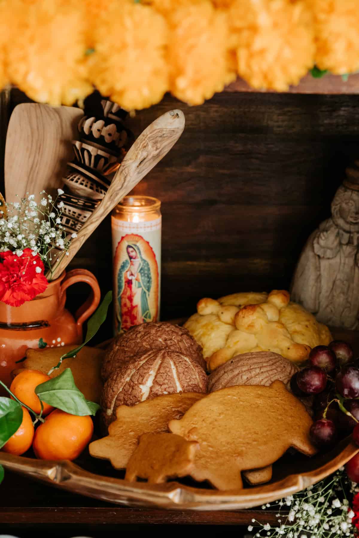 wooden bowl filled with different Mexican pan dulces like marranitos and conchas on a table with fresh grapes and mandarin oranges. 