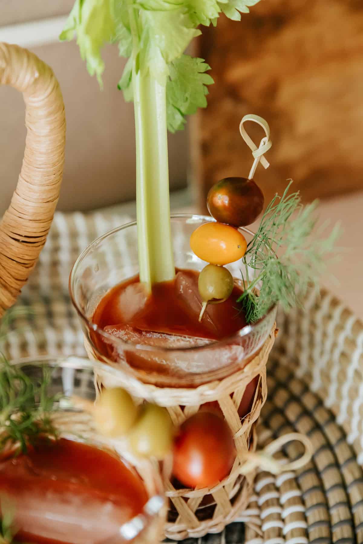 45 degree angle of a bloody maria cocktail on a serving tray with a fresh celery stick, a fresh sprig of dill, and a skewer with a red cherry tomato, yellow cherry tomato, and green olive as garnish.