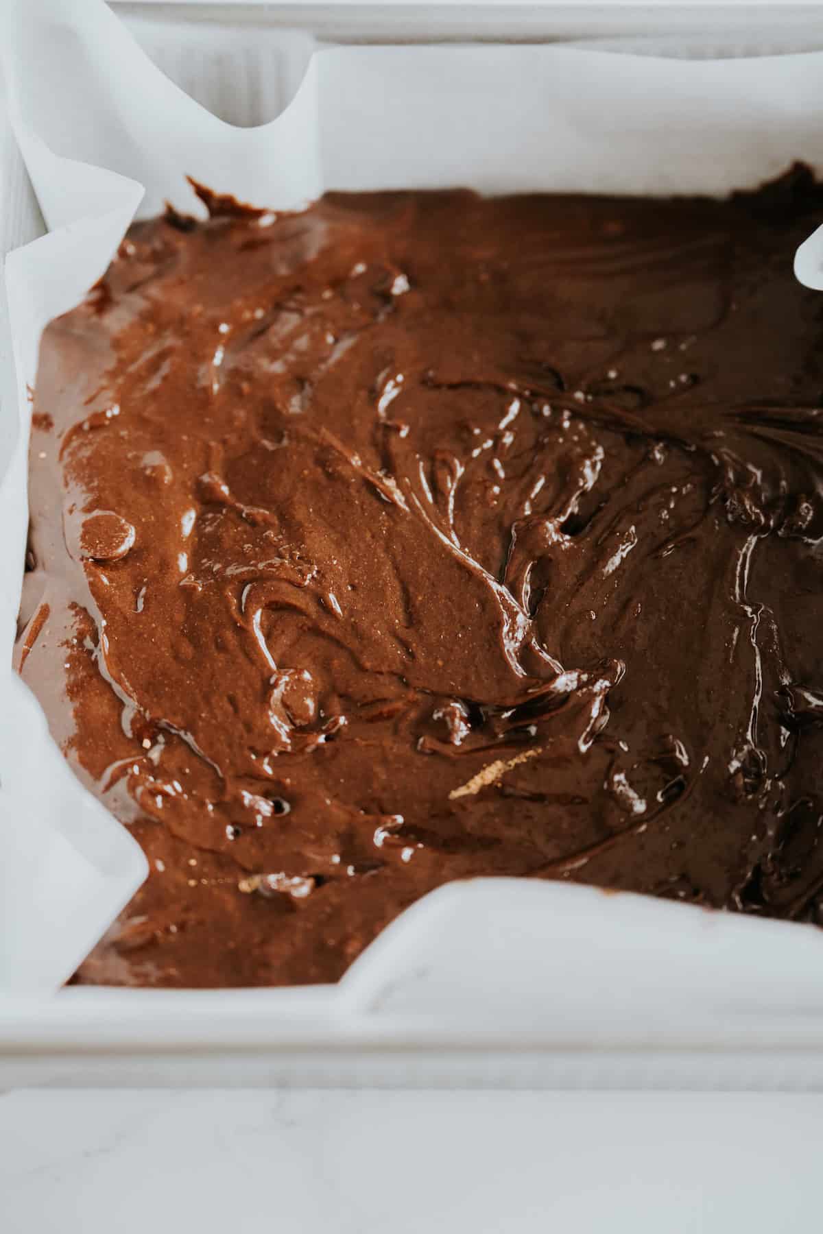 Brownie batter on a prepared pan lined with parchment paper.