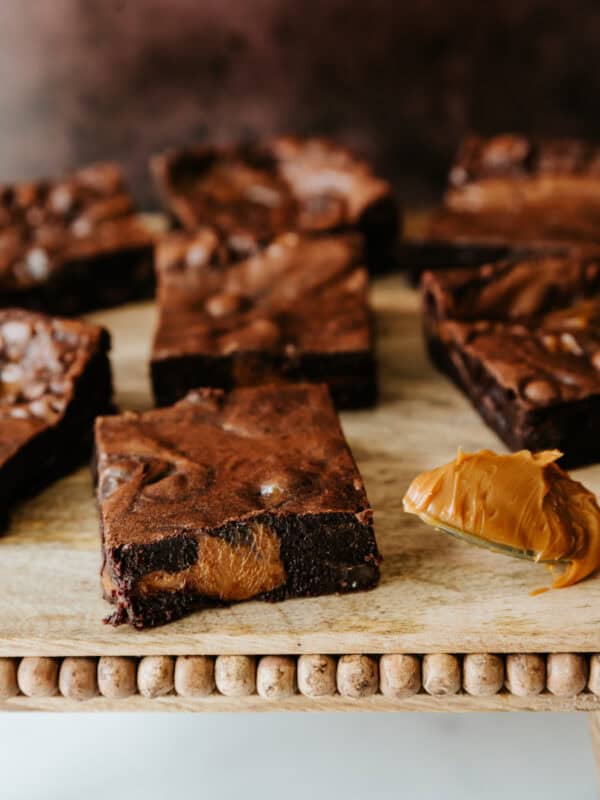 Dulce de leche brownie squares on a wooden pedestal with a brown background.