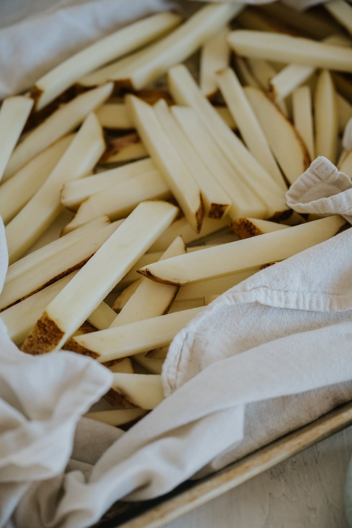 soaked potato rods on a towel-lined baking sheet with some of the towel being pressed atop the top layer. 