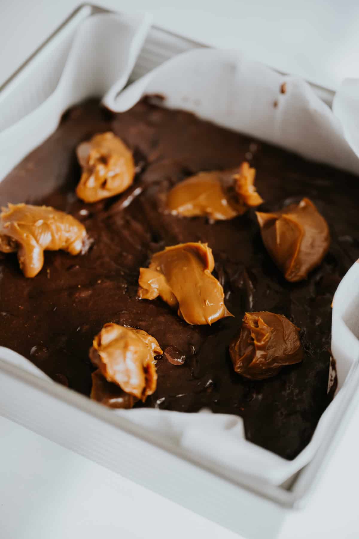 Dollops of dulce de leche on brownie batter in a pan.