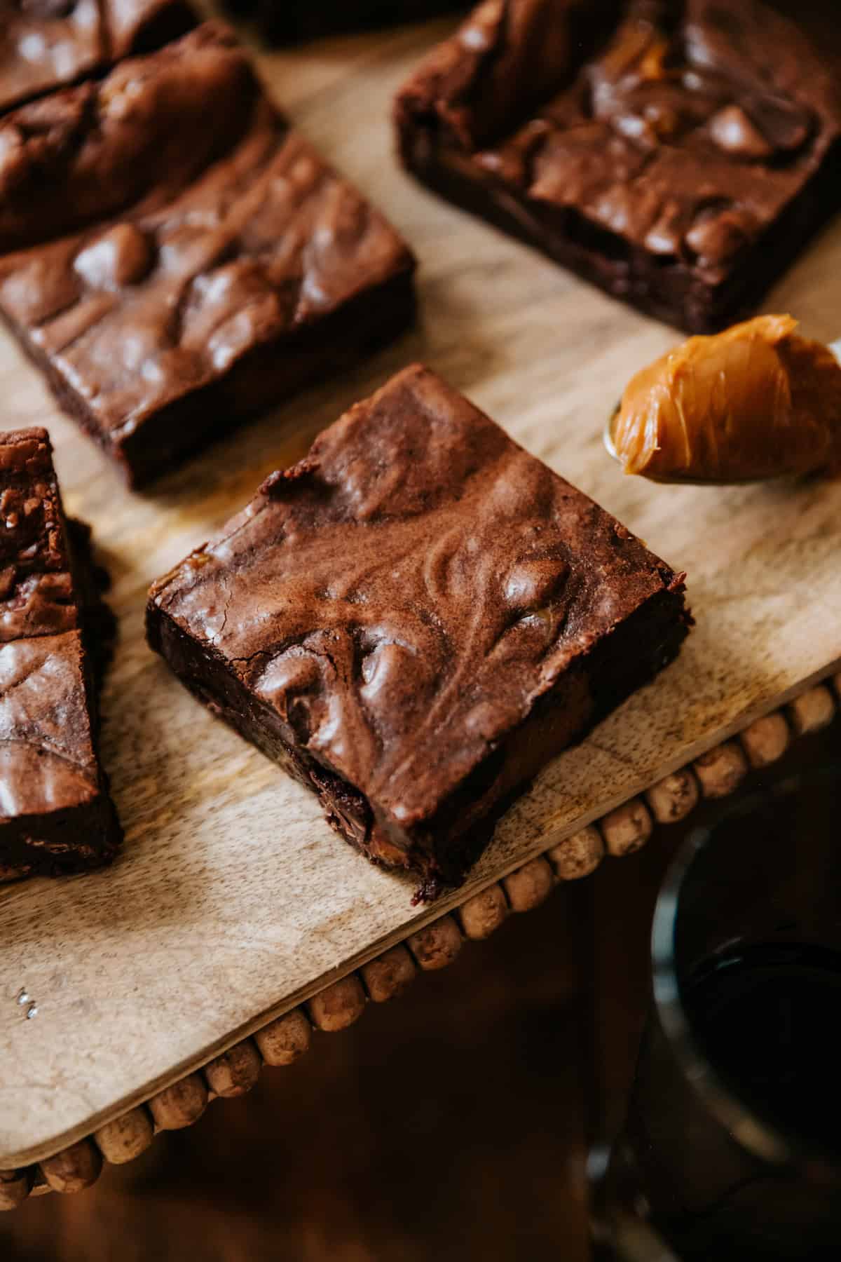 Close up view of dulce de leche brownie squared on a wooden surface with a spoonful of dulce de leche on the side.