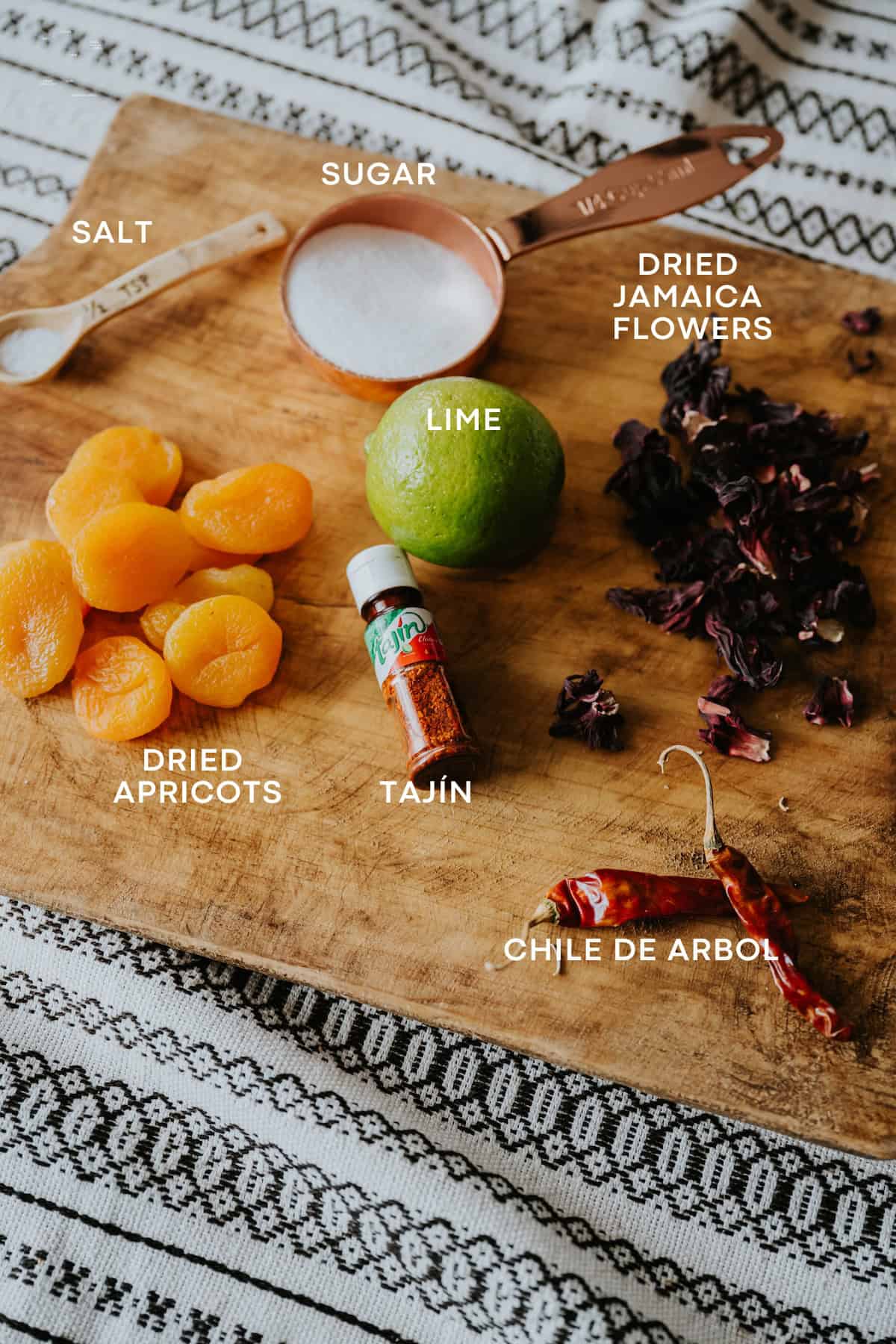 Homemade Mexican Chamoy Sauce ingredients like dried apricots, dried jamaica, sugar and seasonings on a wooden board.