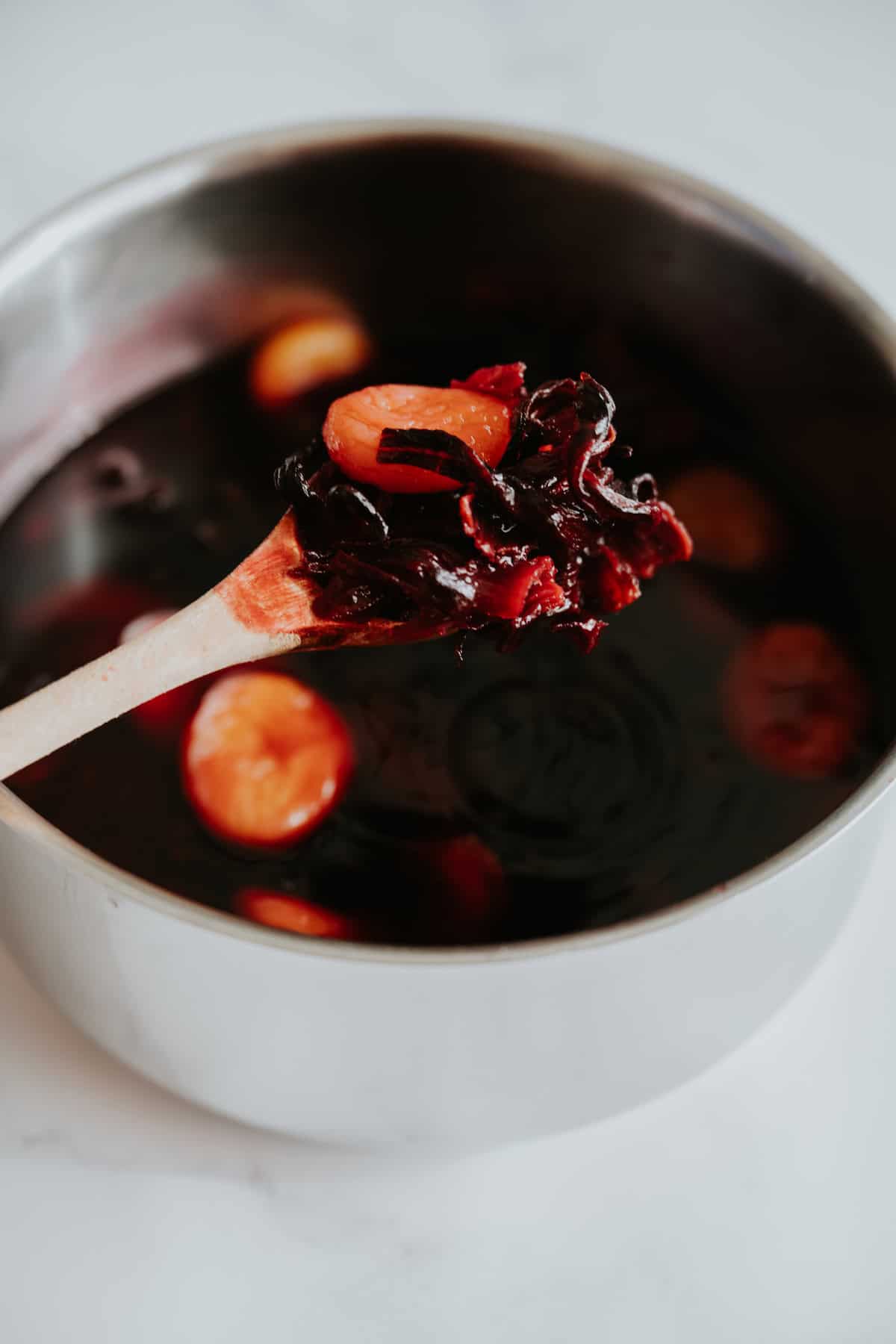 Homemade Mexican Chamoy Sauce in a pot and a wooden spoon is showing simmered apricots and hibiscus.