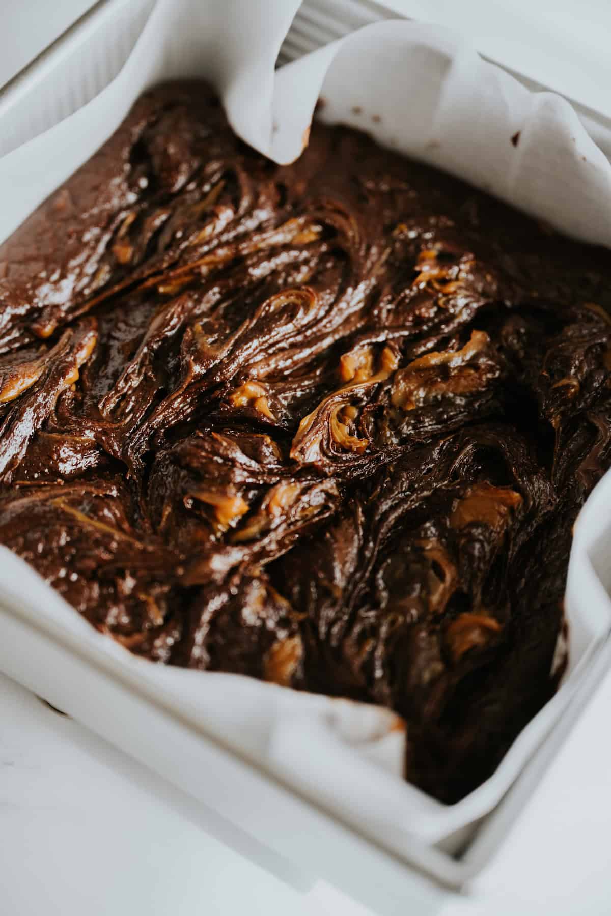 Swirled dulce de leche in brownie batter in baking pan.