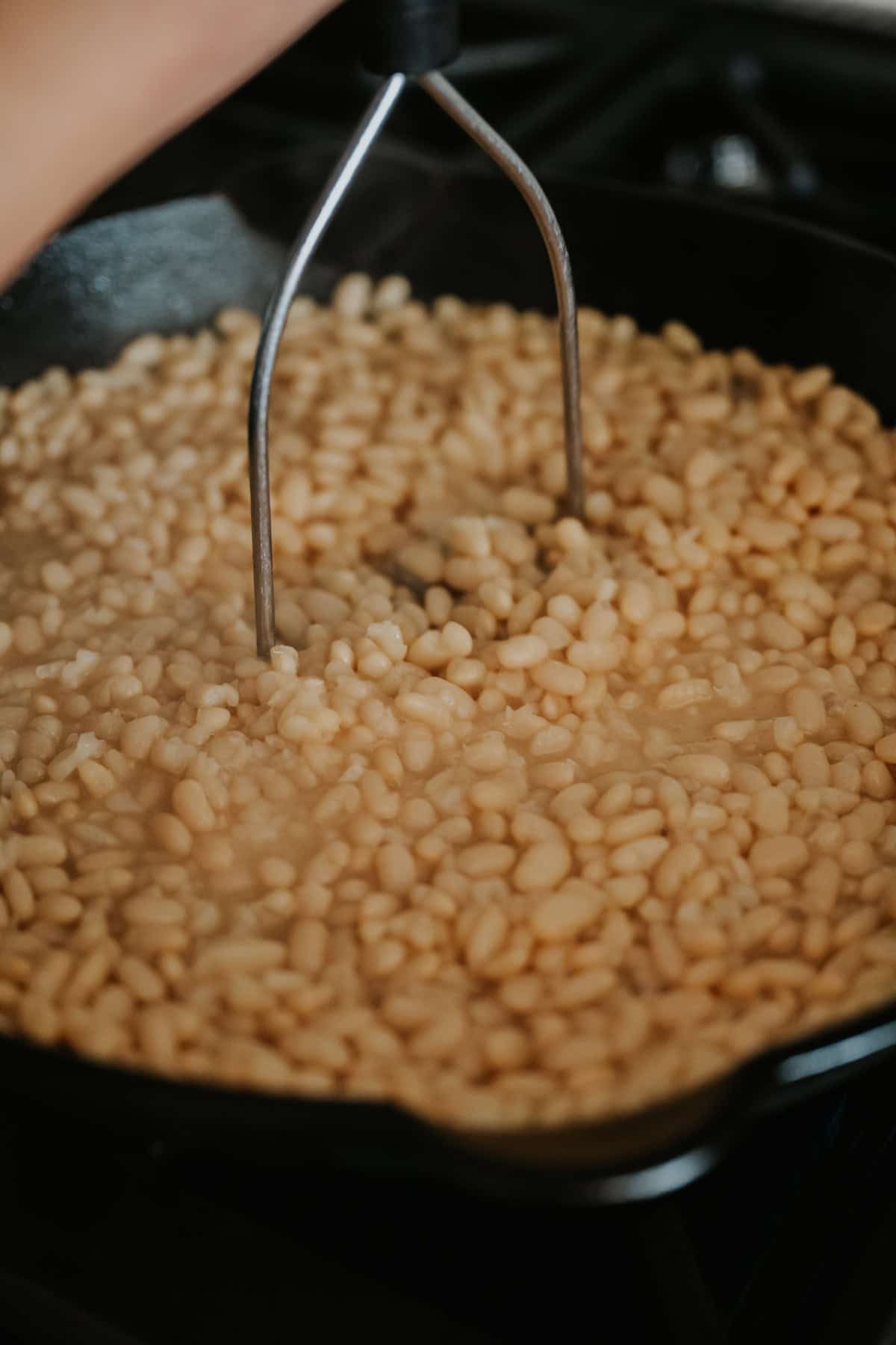 hand using a potato masher to smash the refried white beans. 