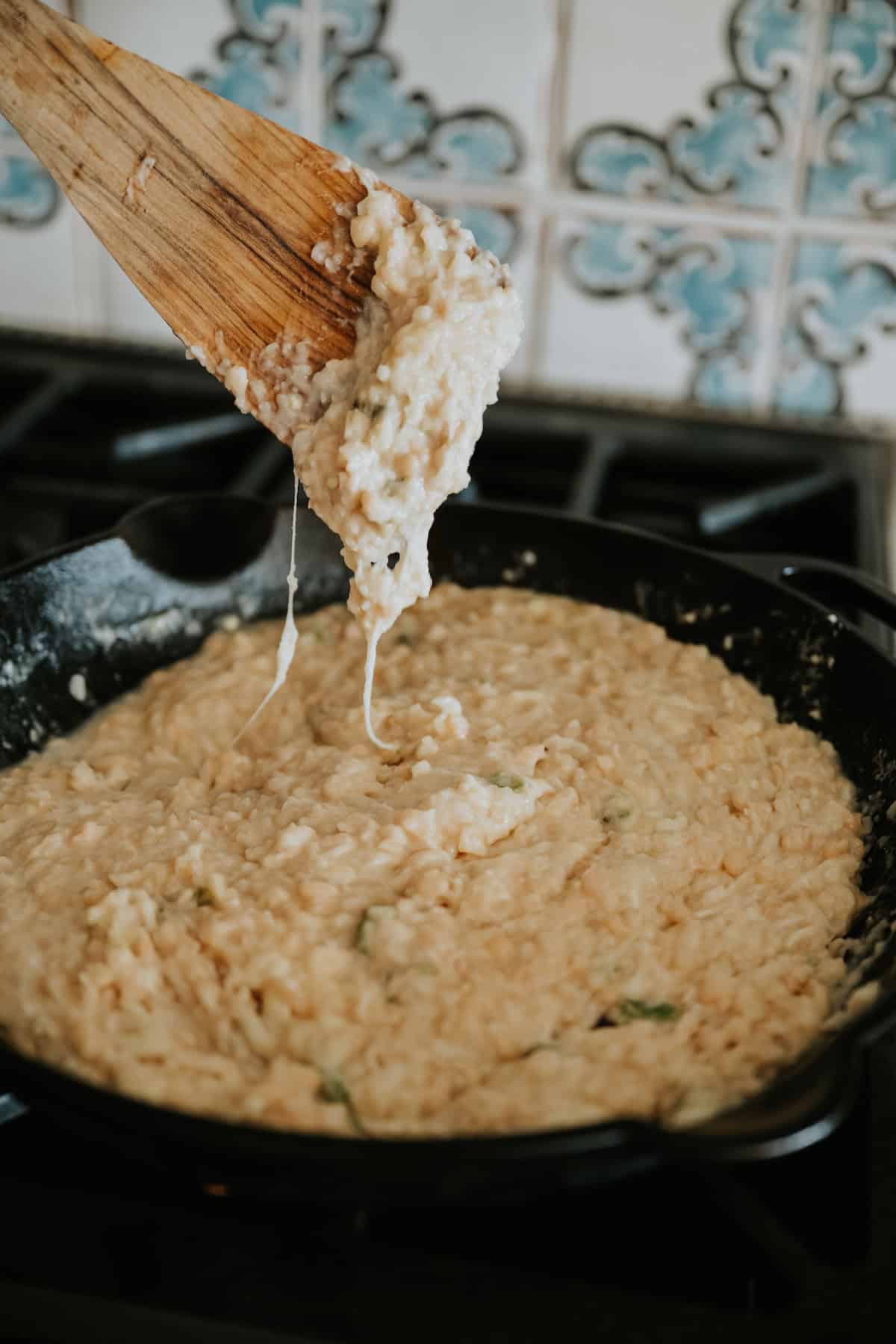 wooden spoon showing the cheese pull from the white refried bean dip after stirring in the cheese and peppers. 