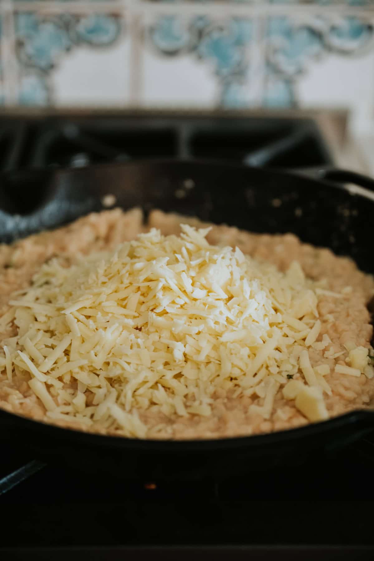 pile of freshly shredded cheese placed atop the refried beans in the skillet. 