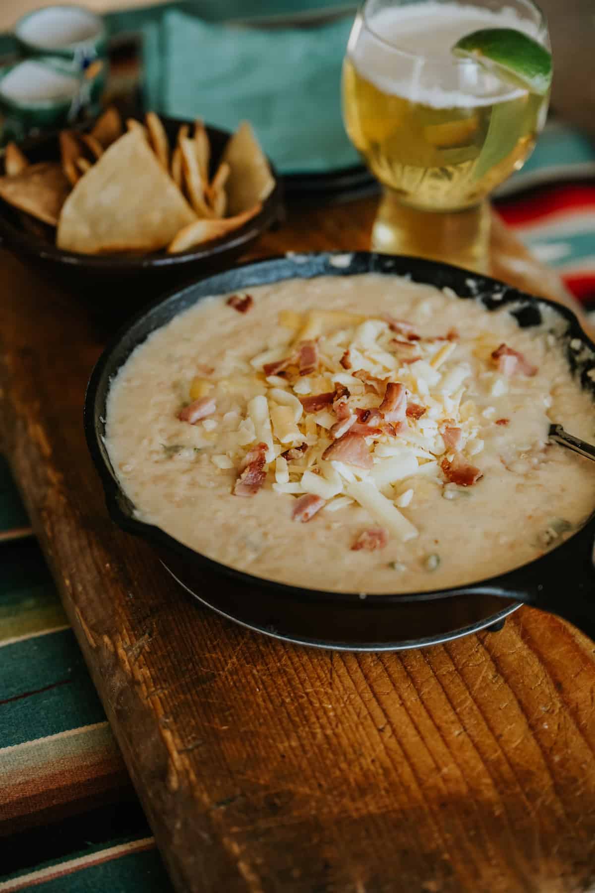 black cast iron skillet filled with refried white bean dip topped with extra melty cheese and extra bacon bits on a wooden table. 