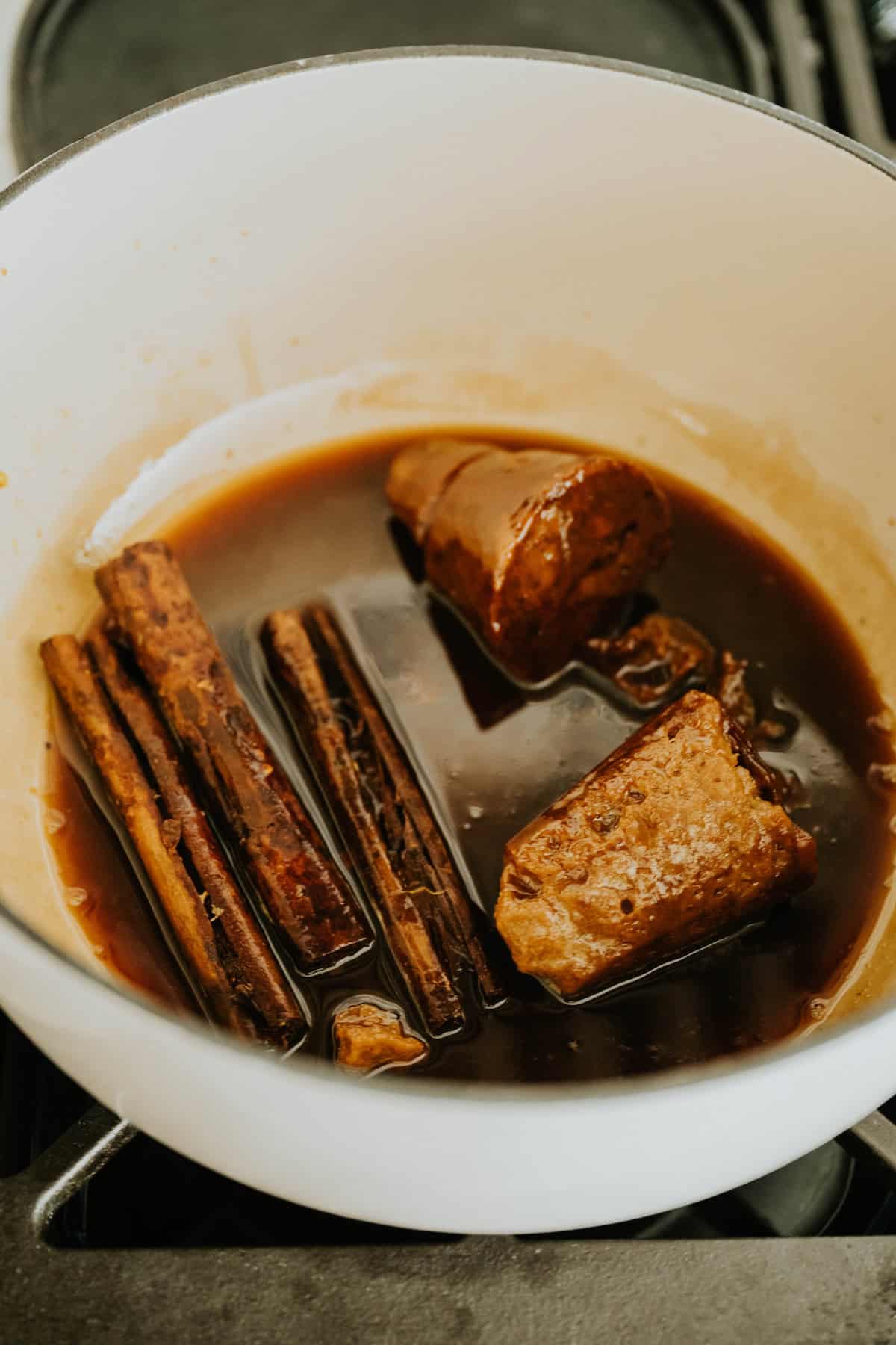 Cinnamon sticks and piloncillo simmering in syrup inside a pot.