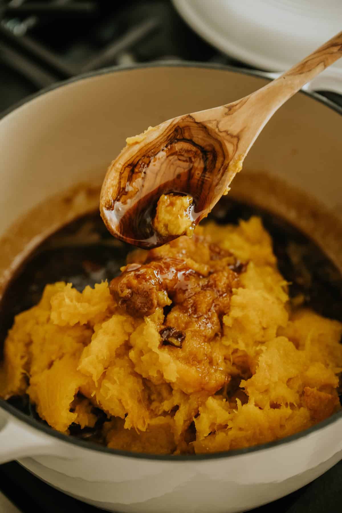 Cooked pumpkin mashed in a clay bowl with a wooden spoon.