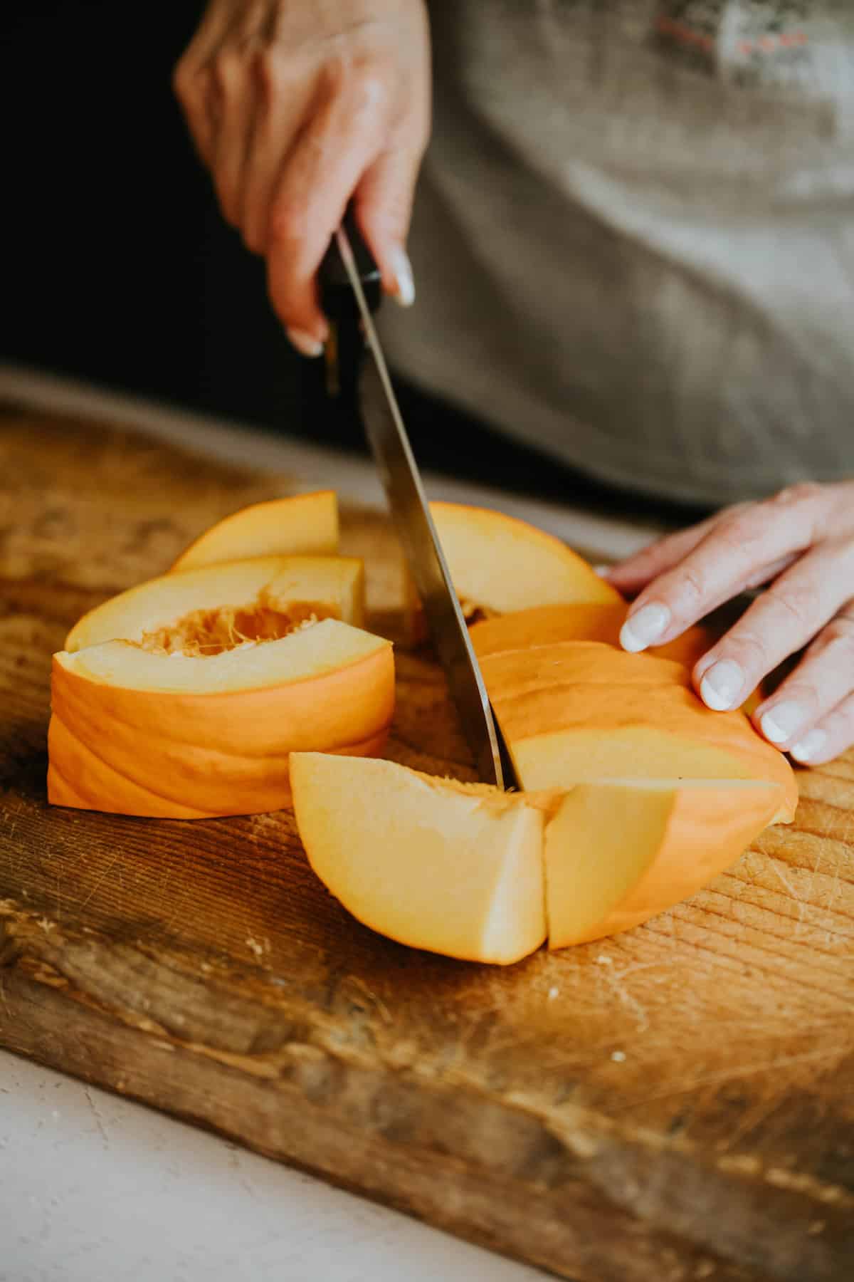 Hands slicing a fresh pumpkin on a wooden cutting board.