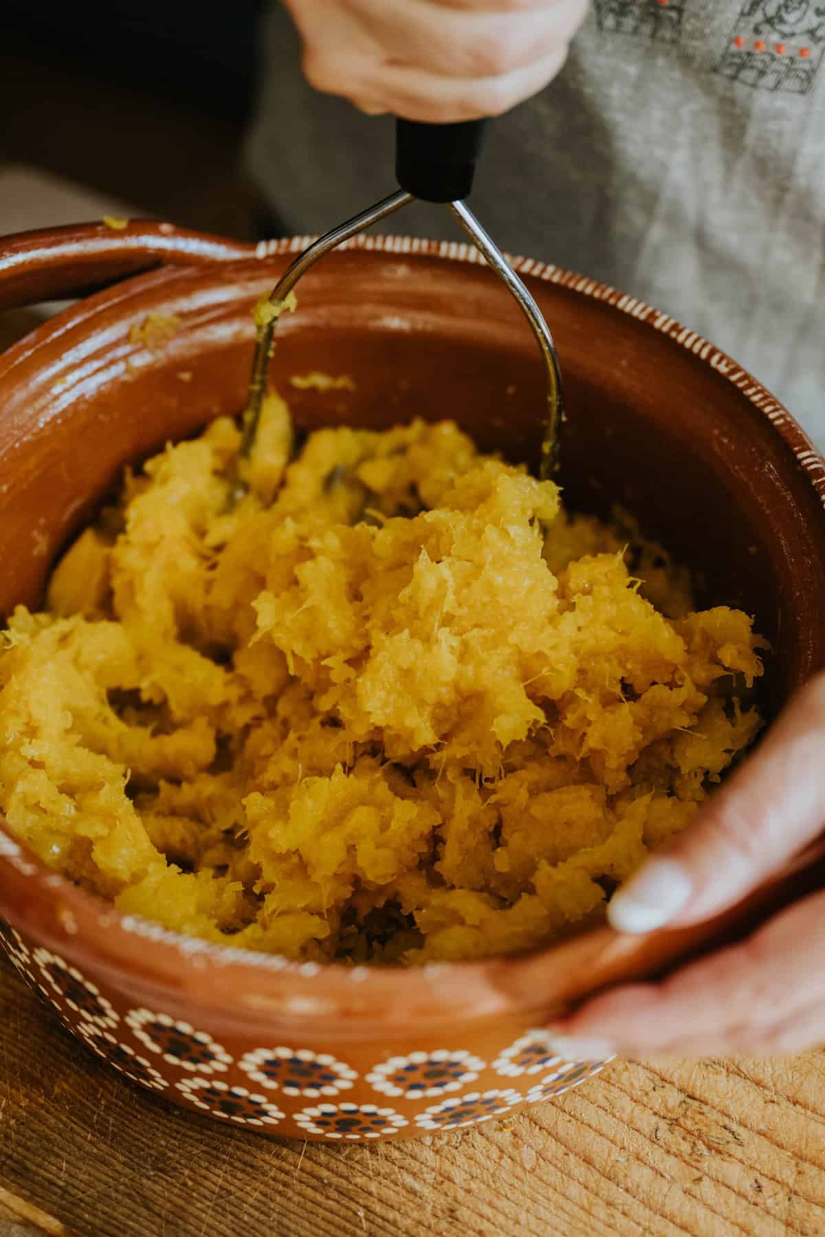 Cooked pumpkin mashed in a clay bowl with a potato masher.