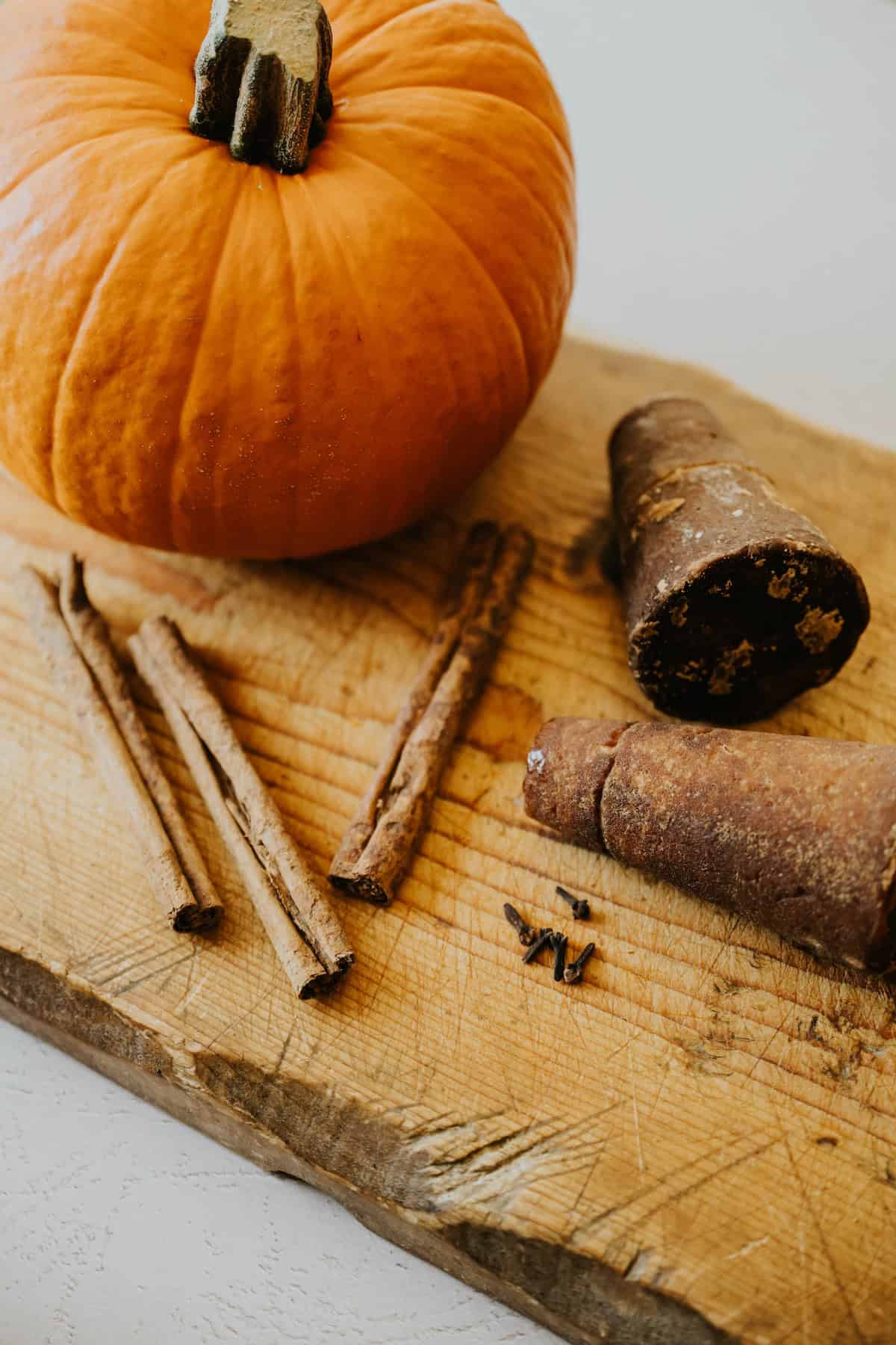 Whole pumpkin with piloncillo, cinnamon sticks, and cloves displayed on a cutting board.