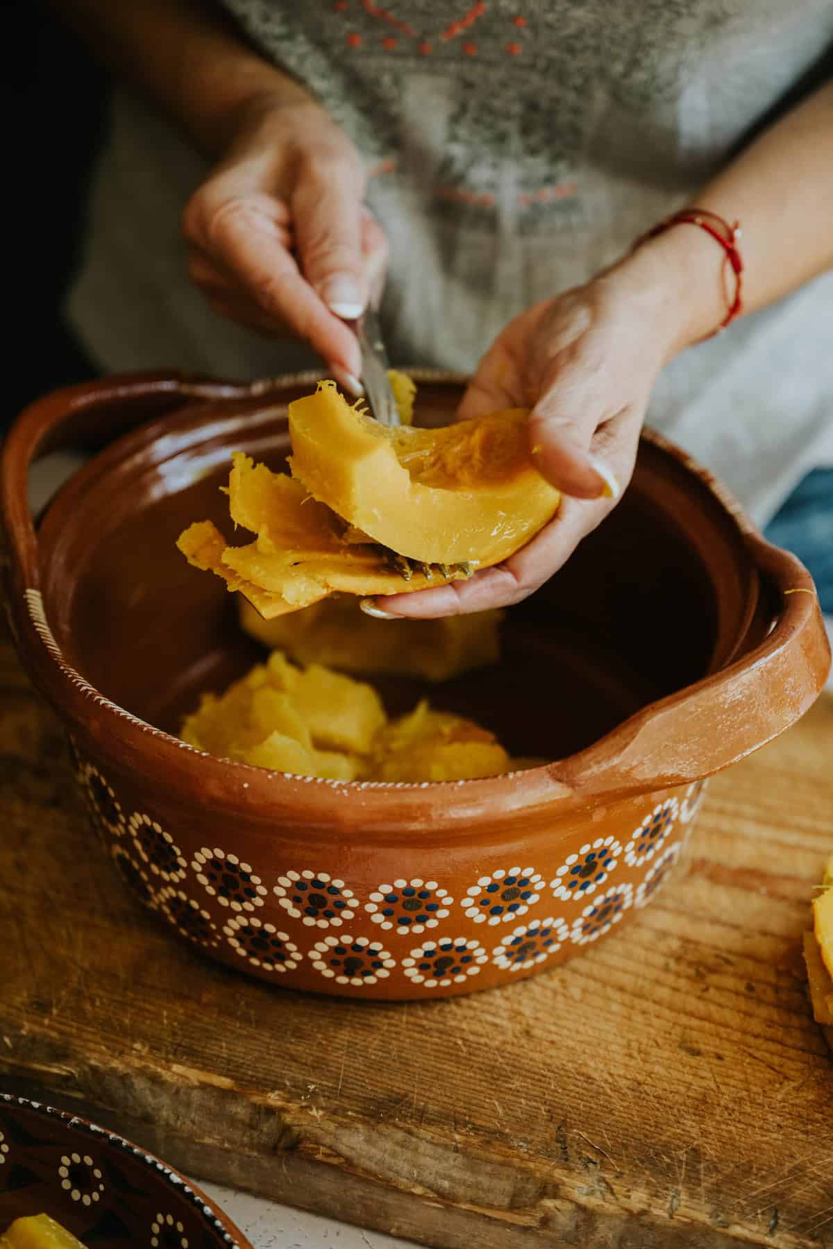 Hands peeling tender cooked pumpkin over a clay dish.
