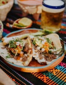 Crispy Cheese Carne Asada Tacos served on a clay plate with grilled cebollitas, salsa, and a cold chelada.
