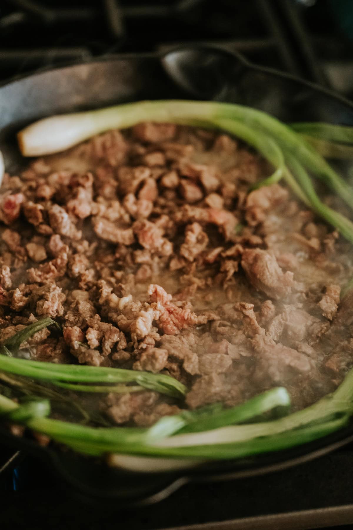 Seasoned taco meat cooked in a skillet with grilled cebollitas.