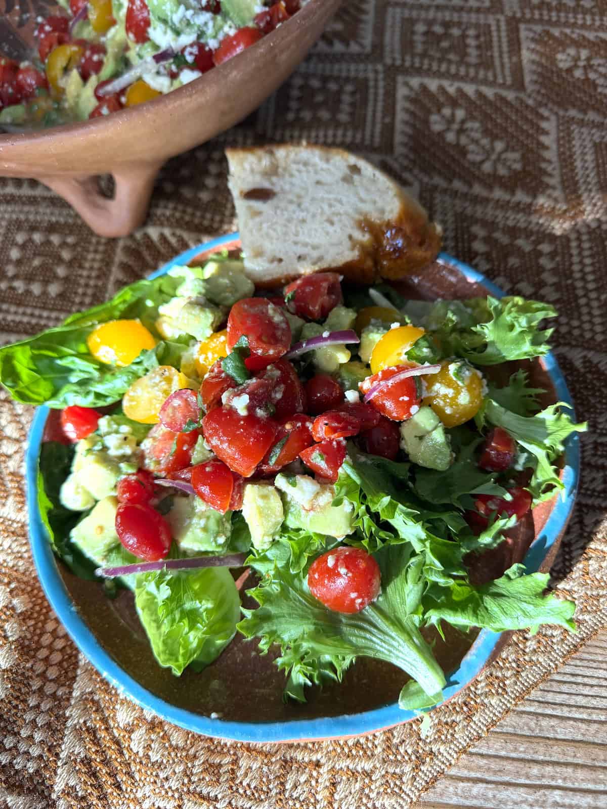 Mexican avocado salad (Ensalada de Aguacate) with colorful cherry tomatoes, creamy avocado, red onion, queso fresco, and cilantro served over fresh greens in a rustic bowl.
