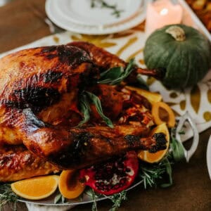 Whole Mexican roast turkey with golden-brown skin served on a platter with orange slices, fresh herbs, and festive Thanksgiving side dishes.