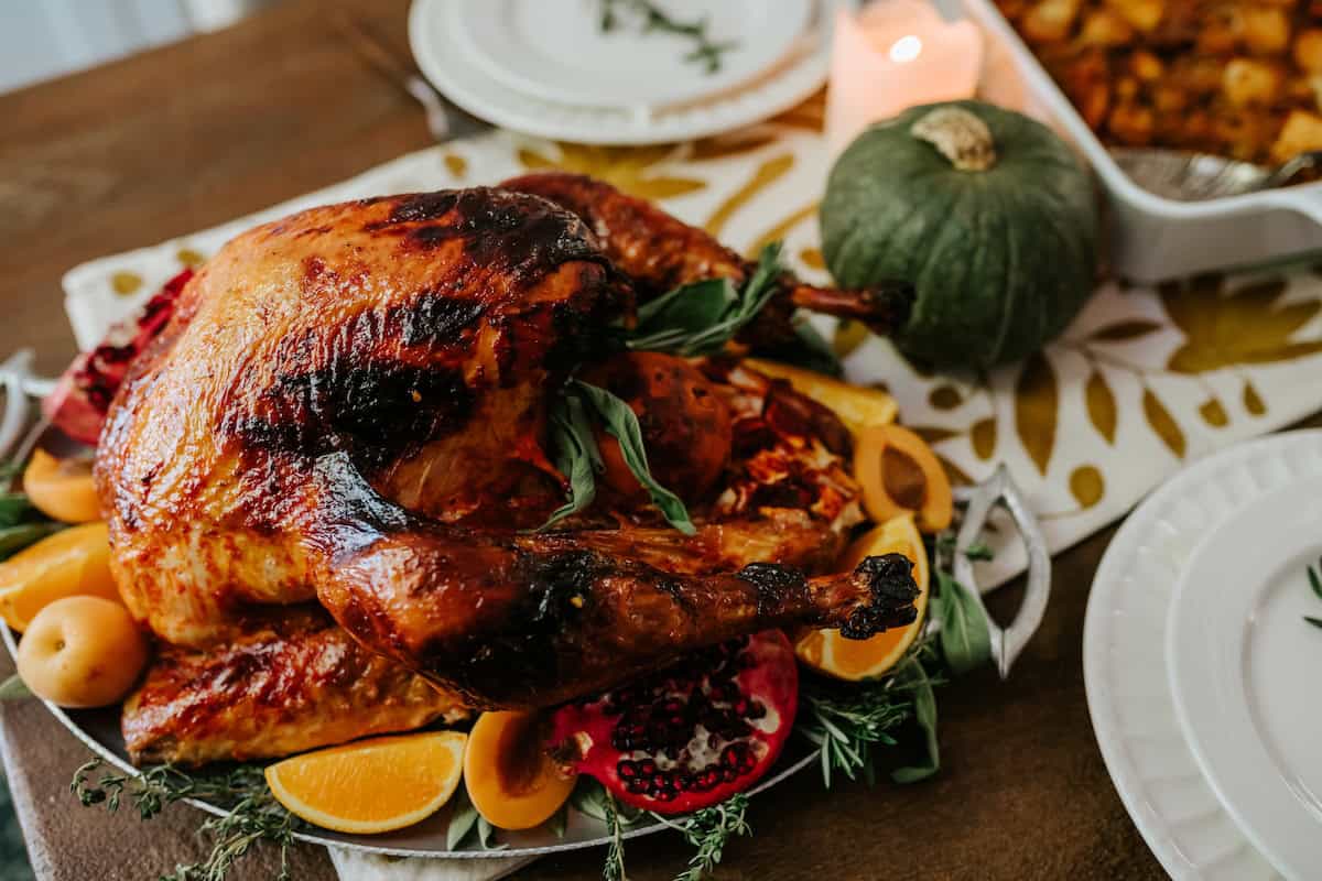 Whole Mexican roast turkey with golden-brown skin served on a platter with orange slices, fresh herbs, and festive Thanksgiving side dishes.