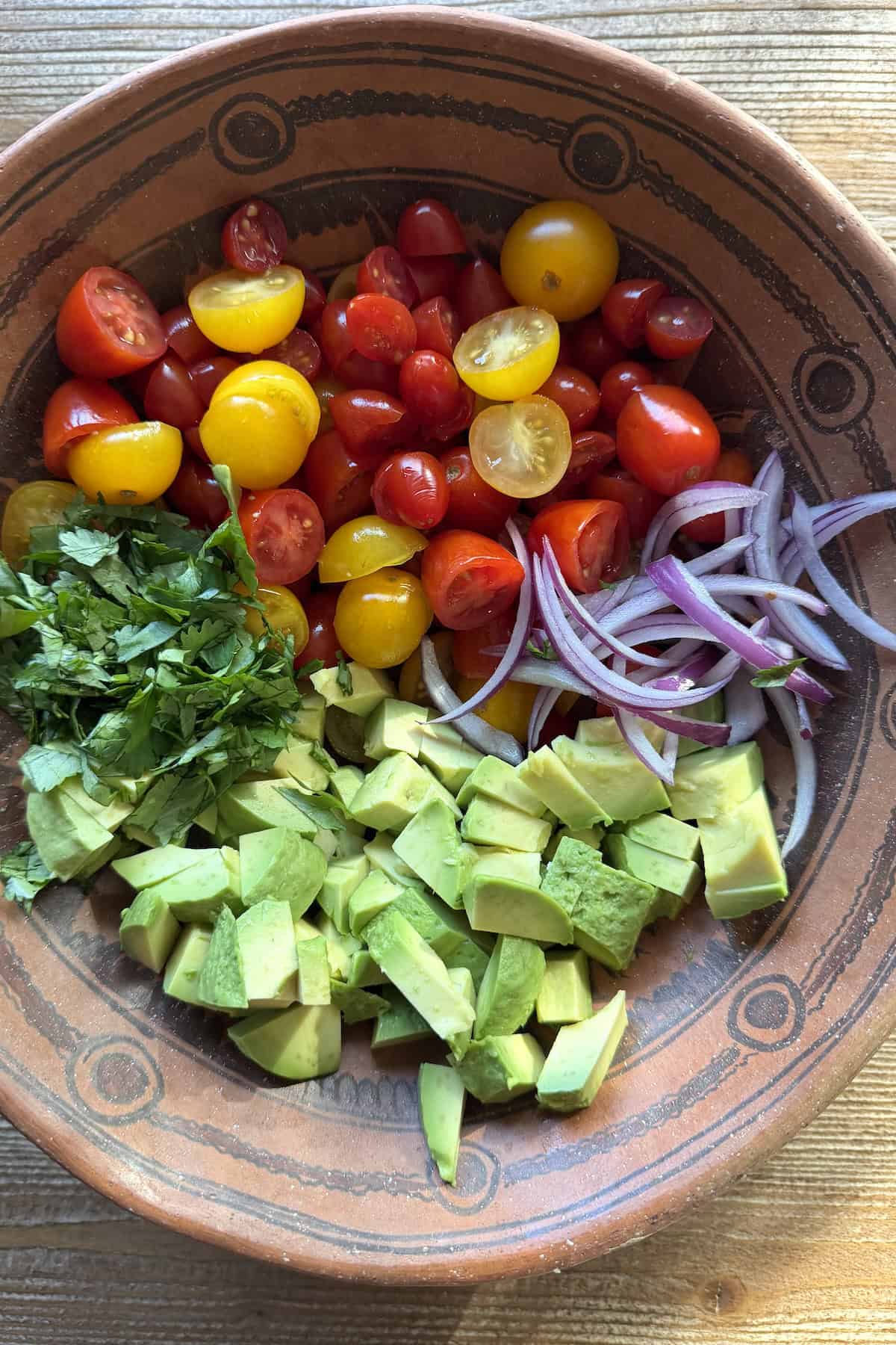 Halved red and yellow cherry tomatoes, diced avocado, thinly sliced red onion, and chopped cilantro arranged in a Mexican clay bowl before dressing.